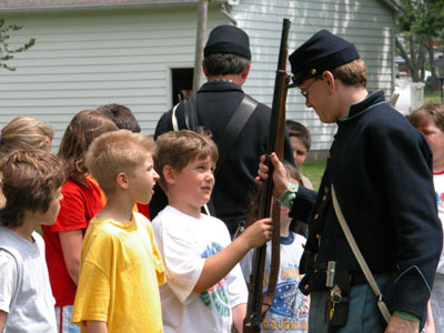 A Civil War re-enactor, dressed in full uniform, hands his musket to a St. Marys fifth-grader to check out at one of nine learning stations outside East elementary school Friday.<br>dailystandard.com