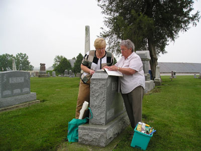 Carolyn Brandon and Karen Miller Bennett review data with their supplies at their feet while working on gathering gravestone information in a local cemetery.<br>dailystandard.com