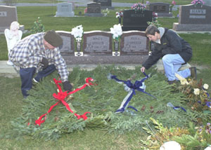 Russell and Annette Spindler, 607 W. Columbia St., Rockford, spread evergreen blankets over their sons' graves at Riverside Cemetery. The couple have lost all three of their children to Duchenne muscular dystrophy during an 11-year period. Sixteen-year-old Regis Spindler left behind a gift list containing video games and a white Christmas tree upon which to hang blue ornaments before his Nov. 27 death.<br>dailystandard.com