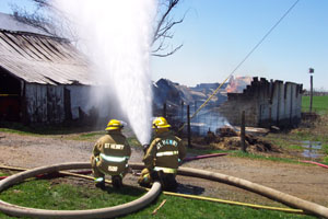 Two St. Henry firefighters direct water toward a frame building containing a 1,000-gallon propane tank Wednesday afternoon. It was one of two buildings destroyed by fire at the home of Mark Evers, 3510 Lange Road, St. Henry. A spark from a lawnmower has been cited as the possible cause of the blaze, which drew 10 area departments.<br>dailystandard.com