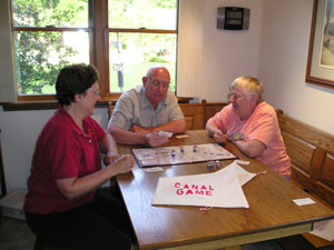 Playing the Canal Game earlier this week around the kitchen table are Jen Conradi, left, Conradi's husband Dennis Dicke and Delores Stienecker. The stops on the board and the game pieces related to bits of New Bremen and canal history. <br>dailystandard.com