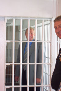Mercer County Commissioner Jim Zehringer peers from a holding area at the Mercer County Jail as Sheriff Jeff Grey looks on. <br>dailystandard.com