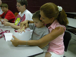 Deb Ahrns, a teacher at the ABC Center in New Bremen, helps her student, 2-year-old Calen, place a label on one of the jugs to be used to raise funds for victims of Hurricane Katrina.<br>dailystandard.com