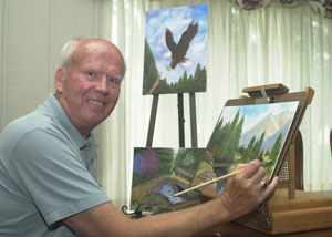 Minster resident Bob Huecker prepares to put the finishing touches on a mountain scene with other examples of his handiwork in the background. He turned to oil painting after retiring from a full-time job at Stolle Corp. in Sidney. Huecker also spent more than 30 years photographing weddings and anniversary celebrations both near and far.<br>dailystandard.com
