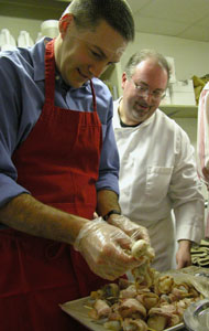 Steve Eiting, complete with hair net, gets a little instruction from Chef Matt Baker on how to place bacon-wrapped scallops onto skewers during a cooking class Saturday night at Haus der Eleganz in Minster. After three hours of the cooking class, Eiting and four other men served an elegant meal to their wives as a Valentine's Day gift.  <br></br>dailystandard.com
