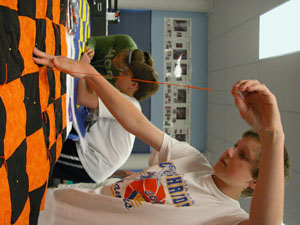 Michael Wiley pulls a long string through the Bengals quilt he's making for art class at Holy Rosary Catholic School in St. Marys. Behind him, Nick Wilker and Maddie Goodwin work on a Roughriders quilt.<br></br>dailystandard.com