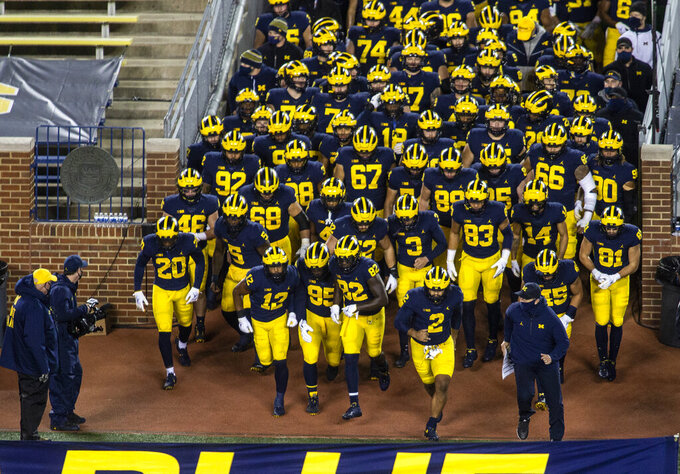 FILE - Michigan head coach Jim Harbaugh, bottom right, leads his team out of the Michigan Stadium tunnel before an NCAA college football game against Wisconsin in Ann Arbor, Mich., Nov. 14, 2020. Michigan Stadium's tunnel will be a little wider next season. The school confirmed Monday, Jan. 23, 2023, that it will remove a portable section of seats from the front of the tunnel to give players, coaches and staff members more room to enter and exit the football field. (AP Photo/Tony Ding, File)