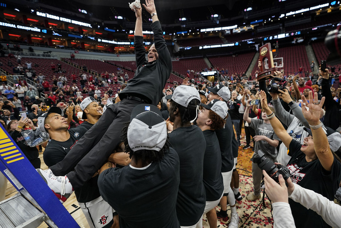 San Diego State head coach Brian Dutcher holds the remains of the net and is falls into the arms of his team after a Elite 8 college basketball game between Creighton and San Diego State in the South Regional of the NCAA Tournament, Sunday, March 26, 2023, in Louisville, Ky. San Diego State won 57-56. (AP Photo/Mike Stewart)
