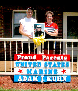 Jim and Brenda Kuhn pose outside their Celina home with the colorful and patriotic sign made to honor their son, Adam J. Kuhn, who is serving in Iraq with the U.S. Marines. The Kuhns' longtime friends, Cheryl and Phil Fennig, also of Celina, said they gave the Kuhn's the unique sign as a gift out of friendship and personal pride for all U.S. military men and women serving their country.<br>dailystandard.com