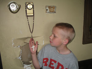Young Michael Bruns inspects the beaded rosary that survived a March blaze at his home near Egypt. Neither the rosary nor the thermostat it encircles were damaged even though nearby thermostats melted. Firefighters made the hole behind it while checking for flames between the walls. <br></br>dailystandard.com