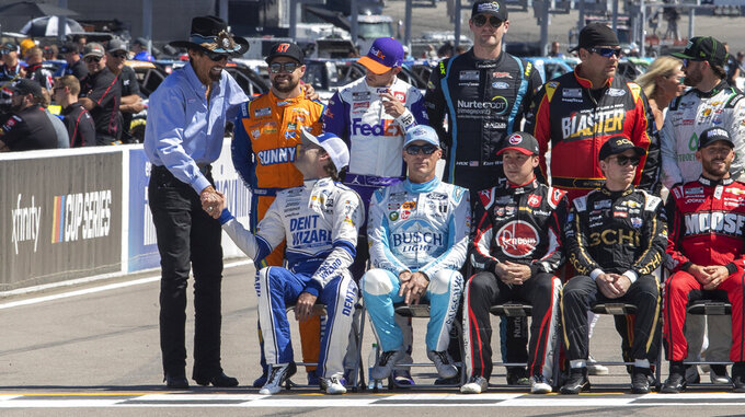 Richard Petty talks with NASCAR drivers, including Ryan Blaney, lower left, and  Ricky Stenhouse Jr., upper left, before a group photo Friday, June 3, 2022, to promote the NASCAR Cup Series auto race at World Wide Technology Raceway in Madison, Ill. Petty won the Cup championship seven times. (Derik Holtmann/Belleville News-Democrat via AP)